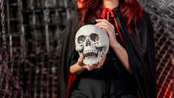 Beautiful woman wearing witch costume holding a human skull in halloween theme. Focus skull photo