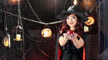 hermosa joven asiática vestida de negro con sombrero de bruja sosteniendo manzana en el tema de halloween. cara de enfoque foto