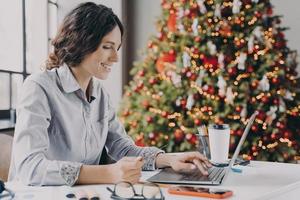 Young Europian woman using laptop at Christmas, enjoying online shopping during holiday season photo