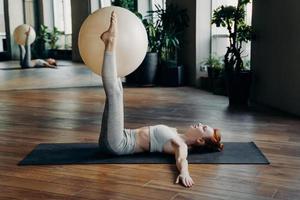 Woman holding exercise ball with straight legs on yoga mat photo