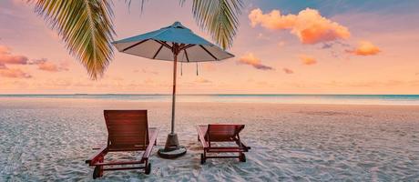 Beautiful tropical sunset beach. Romantic couple goals, two sun beds, umbrella under palm tree leaves. Panoramic coast landscape, love and relaxation banner. Colorful dream travel sea sand sky island photo