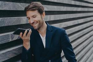 un joven atractivo se para afuera y usa un asistente de reconocimiento de voz en un teléfono inteligente foto