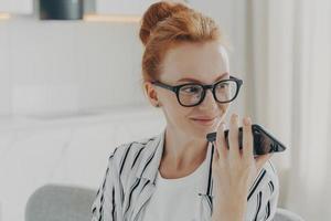 Horizontal shot of ginger woman uses voice assistant on smartphone makes voice call photo