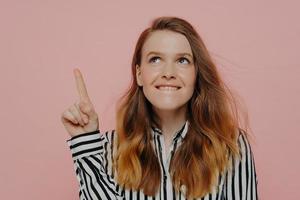 Young woman thinking while biting lips and having pointer finger up photo