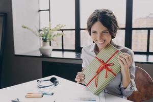 dama alegre empleada de oficina mirando la pantalla sonriendo ampliamente mostrando a la cámara de la computadora regalo de navidad foto