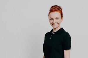 Headshot of young positive millennial red haired woman looking at camera with charming smile photo