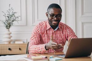 Positive african man online teacher tutor looking at laptop screen and talking with students photo