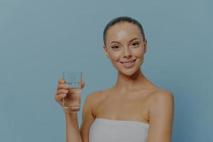 belleza y estilo de vida saludable. joven mujer feliz bebiendo agua mineral pura, aislada en azul foto