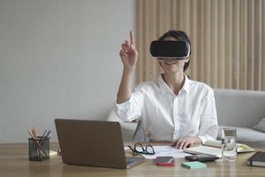 Female office worker in vr headset interacting with digital interface, touching 3d objects photo