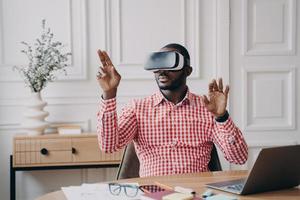Concentrated Afro american businessman using VR headset, experiencing virtual reality playing game photo