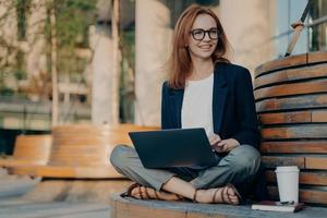 una mujer pelirroja bonita y complacida aprende un curso educativo en una computadora portátil foto