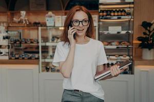 Busy female bakery shop owner has conversation on mobile phone photo