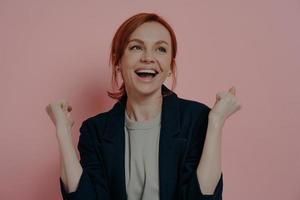 Portrait of happy excited redhead female with raised fists celebrating victory, isolated on pink photo