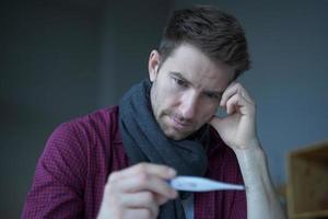 Sick unhealthy German man office worker looking at thermometer, suffer of flu influenza photo