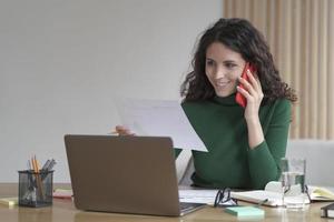 Pleasant Italian businesswoman talking on mobile phone and consulting client while working remotely photo