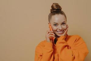 Charming young woman holding cellphone near ear, talking on phone with boyfriend, isolated on beige photo