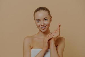 Young attractive woman using handcream to keep skin hydrated, touching hands after paraffin wax bath photo