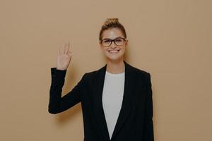 Positive young caucasian woman in classic wear isolated on beige background showing ok sign photo