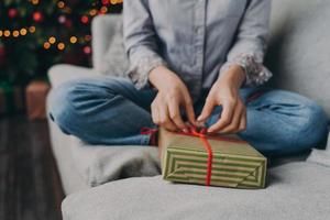 Cropped shot of woman opening wrapped christmas gift box at home during winter holidays photo