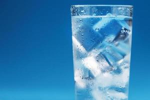 un vaso con agua helada y cubitos de hielo sobre un fondo azul.