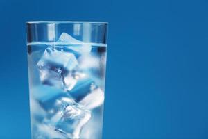 A glass with ice water and ice cubes on a blue background. photo