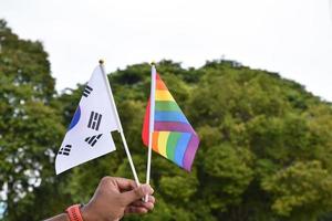 bandera del arco iris y bandera nacional de corea del sur sosteniendo en la mano, enfoque suave y selectivo, concepto para la celebración de lgbtq plus en el mes del orgullo en todo el mundo. foto