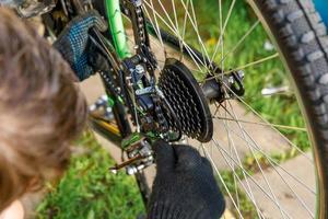 Bike mechanic man repairs bicycle in bicycle repair shop, outdoor. Hand of cyclist bicyclist examines, fixes modern cycle transmission system. Bike maintenance, sport shop concept. photo