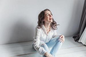 Girl in bright room sitting against white wall photo