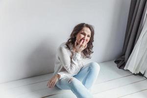 Girl in bright room sitting against white wall photo