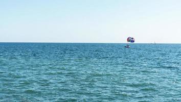 parasailing multicolored rainbow parachute behind boat over blue turquoise sea landscape summer activities copy space selective focus photo