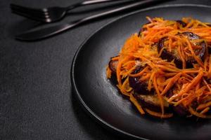 Korean salad with eggplant, carrots, garlic, spices and herbs on a dark concrete background photo