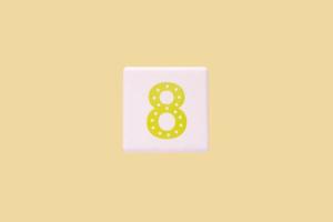 Close-up photo of a white plastic cube with a yellow number 8 on a yellow background. Object in the center of the photo