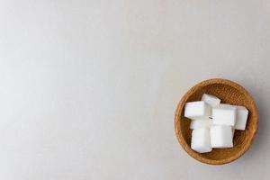 Sugar cubes in a wooden plate on the kitchen table. On right side of the photo. Top view. With copy space photo