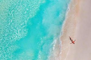 vista aérea de la mujer en la playa en las islas maldivas. vacaciones y aventura. viajes playa turquesa océano agua. vista superior desde drone, mar azul tropical y mujer relajada, despreocupada, libertad, relajada foto