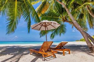 Beautiful tropical island, couple chairs umbrella under palm tree leaves, paradise sea sand sky. Summer travel landscape amazing vacation beach. Idyllic exotic nature closeup of recreation relaxation. photo