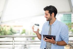 The man holding a cup of coffee and tablet while he is working at the outside of office, Feeling happy and  relaxing. photo