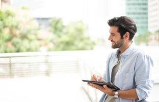 The young man using a tablet to working at out of office. The man wearing casual cloth and feeling relaxing and happy. photo