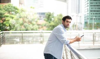 Young caucasian man using smart phone and smiling while waiting his friend at the outside. photo