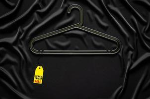 A black hanger with yellow price tag on black smooth and wavy cloth with space for text. Black Friday concept. photo