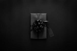 A black gift box with ribbon and price tag puts on black background. Black friday concept. photo
