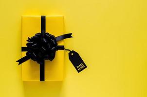 una caja de regalo amarilla con cinta negra y etiqueta de precio se pone sobre fondo amarillo. concepto de viernes negro. foto