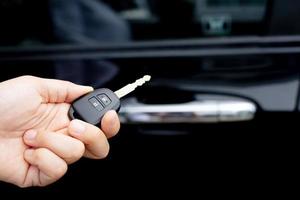 A man holding a car key in front of a car at a showroom photo