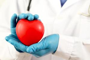 joven doctora sosteniendo un corazón rojo sobre un fondo blanco foto