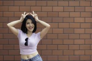 retrato de una chica hipster en el fondo de la pared de ladrillo, hermosa mujer asiática posa para tomar una foto