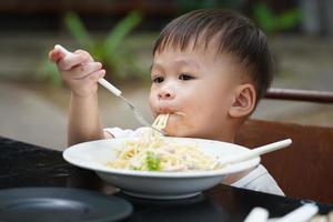 niño pequeño comiendo espaguetis con delicias, concepto de aprendizaje para niños pequeños foto