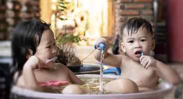 Asian sister and brother taking a shower and brushing their teeth in the bathtub in morning. Happy kids playing and bathing outside the house concept. Take a shower outside on a hot day. photo