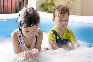 hermanas y hermanos están felices de jugar con burbujas de agua en la piscina inflable. jugando en el agua en casa durante el verano. felicidad familiar, niños jugando en el agua. foto