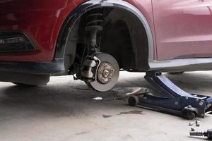 sustitución de la rueda del coche con gato hidráulico. concepto de mantenimiento de automóviles. Retire las ruedas del automóvil en preparación para el parche de neumáticos. discos de freno sin ruedas. centro de servicio de reparación de automóviles foto