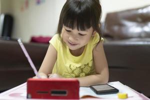 Cute Asian girl using smartphone to study online with teacher on video call at home. homeschooling, distance learning. quarantine concept. online education. photo