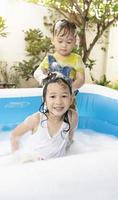 el hermanito estaba lavando el cabello de su hermana en una piscina inflable. niña y niño jugando con pompas de jabón en la piscina en casa. feliz de jugar en el agua durante las vacaciones de verano. foto